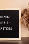 Sign reading “Mental Health Matters” beside a small vase of dried plants on a table.
