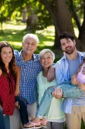 Multi‑generational family standing together in a park, with adults and children gathered close and facing the camera.