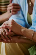 Close‑up of one person holding another person’s hands, with a third person resting a hand on their shoulder nearby.