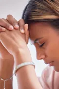Close‑up of a person with hands clasped together near their face and head lowered.