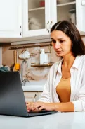 A person sitting at a table in a kitchen using a laptop.