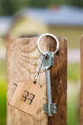 A key with a house-shaped keyring hanging on a wooden fence post.
