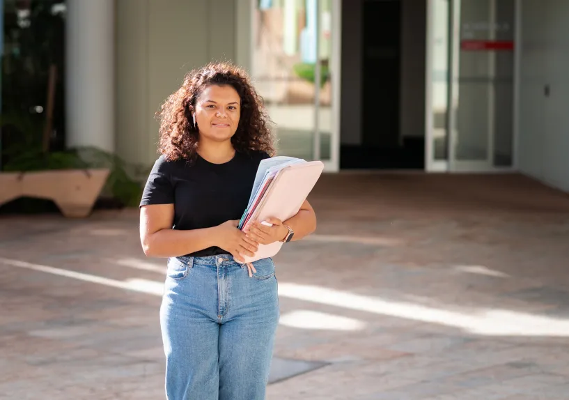 Adult female standing outside a building holding a folder, with doors and a walkway behind.