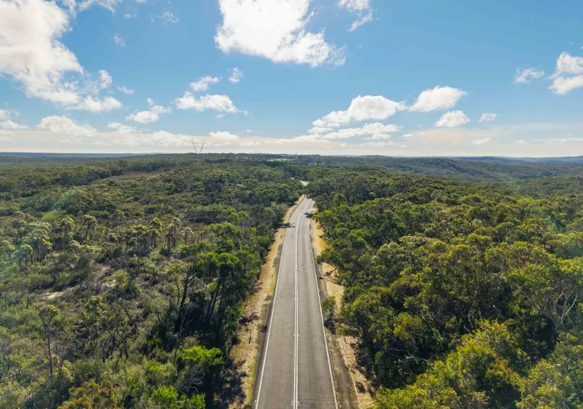 Aerial view of a winding road running through bushland under a blue sky.