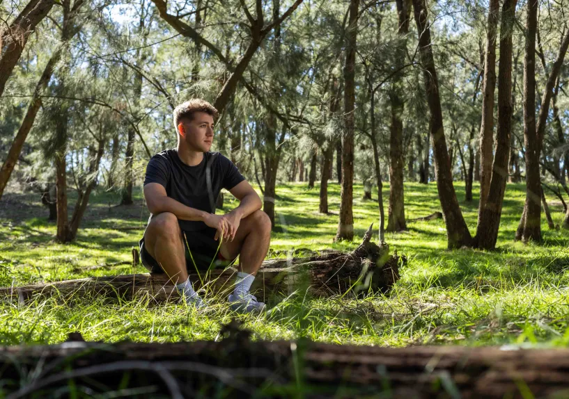 A person sitting on a fallen log in a forest area.