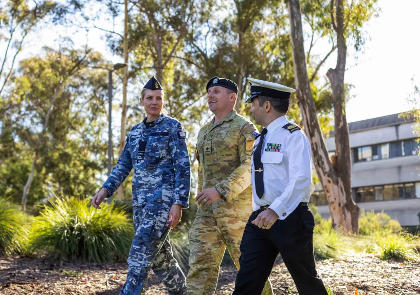 Three people in different Australian Defence Force uniforms walking side by side in a park.