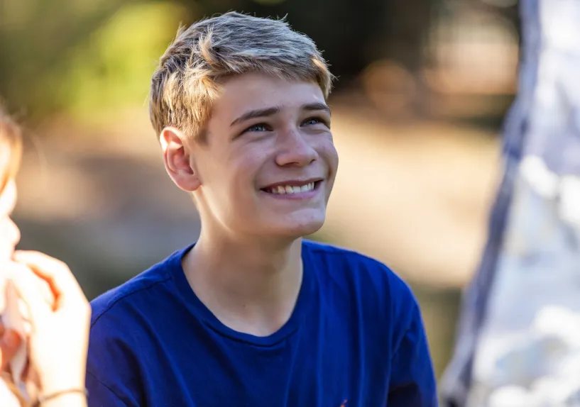 Close-up of teenage boy sitting outdoors, looking up at someone standing nearby.