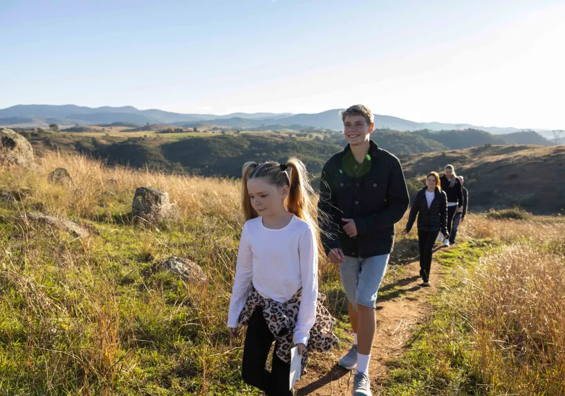 A family hiking together along a narrow path on a grassy hillside.