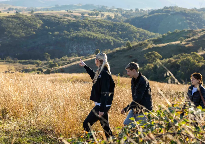 An adult and two teengage children walking together through a grassy hillside landscape, with the adult pointing into the distance.