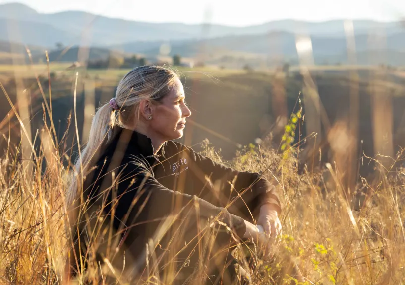 A person sitting in tall grass on a hillside, looking out over the landscape.