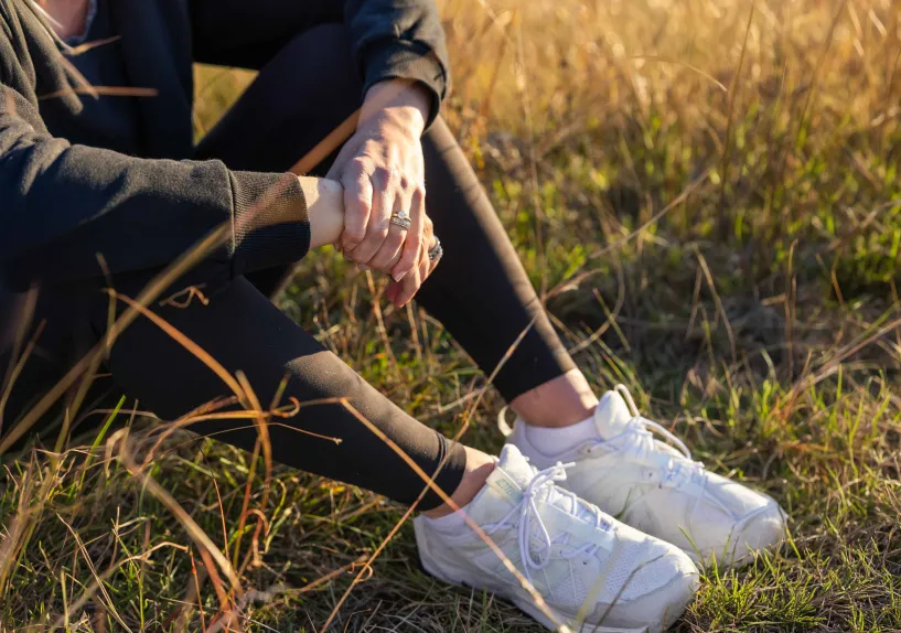 Close-up of a person clasping their hands while sitting in tall grass on a hillside.