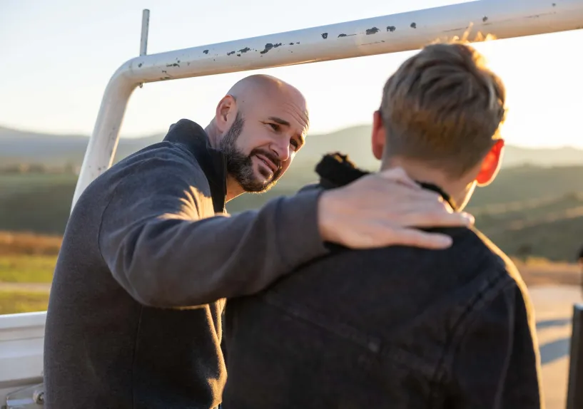 An adult resting a hand on a teenager's shoulder while talking at the back of a vehicle.