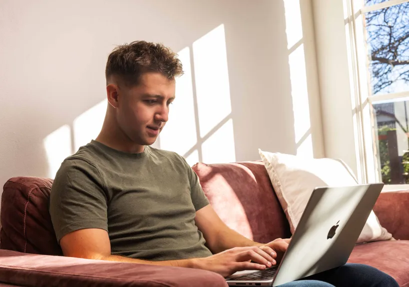 A person sitting on a couch at home using a laptop.