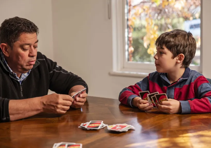 An adult and child sitting at a table playing a card game together.