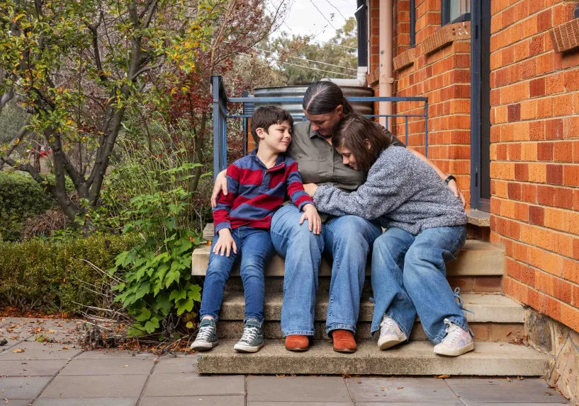 An adult and two children embraced in a cuddle on outdoor steps.