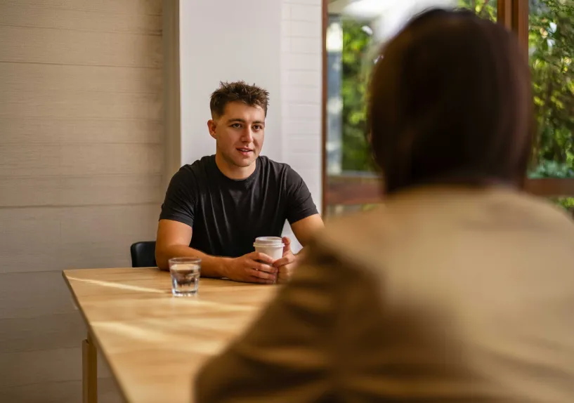 A person catching up over coffee with another person in a relaxed community setting.