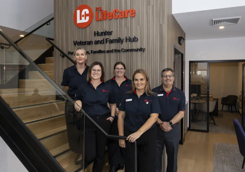 Five staff members in uniform standing together near a staircase inside the Hunter Veteran and Family Hub, with signage on the wall behind them.