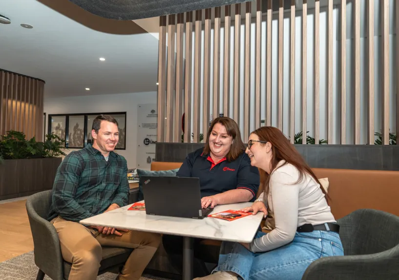 Three people seated at a table inside the Queanbeyan Veteran and Family Hub, looking at a laptop together.