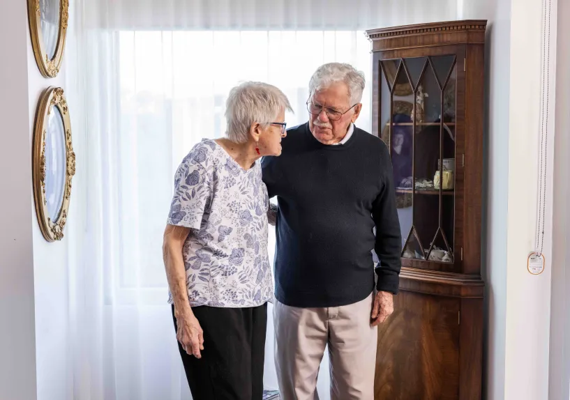 Two elderley people standing close together having a conversation.