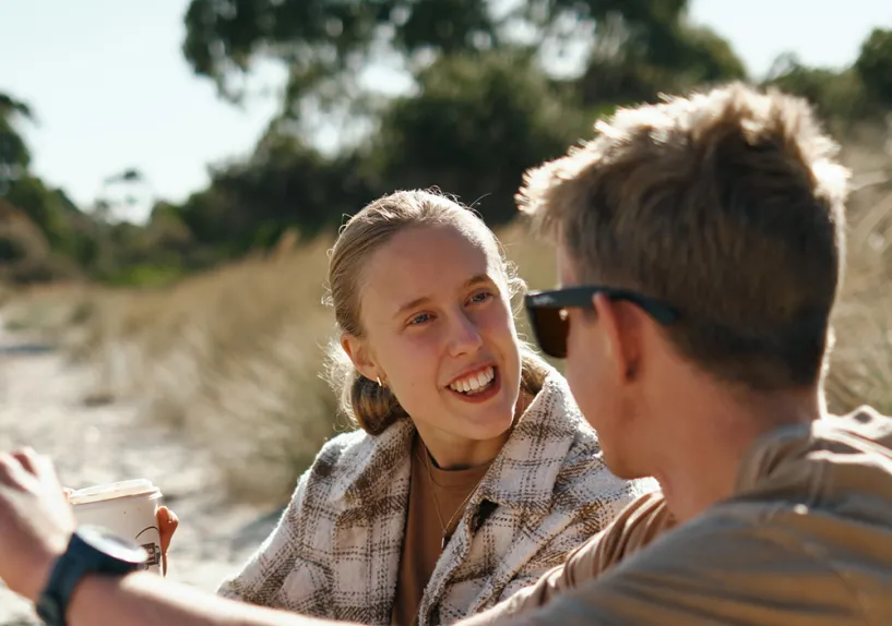 Two people sitting together in conversation on a sandy beach.