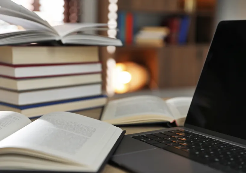 Open books stacked beside a laptop on a desk, with pages spread in a study setting.
