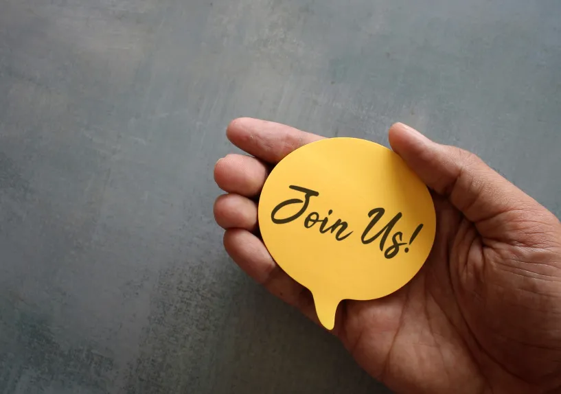 join us-message on yellow note, held in palm of hand - grey background