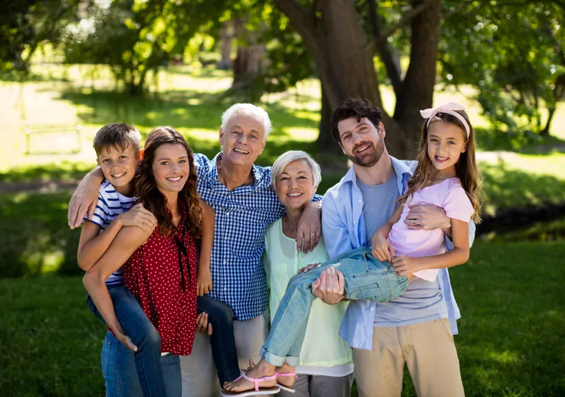 Multi‑generational family standing together in a park, with adults and children gathered close and facing the camera.