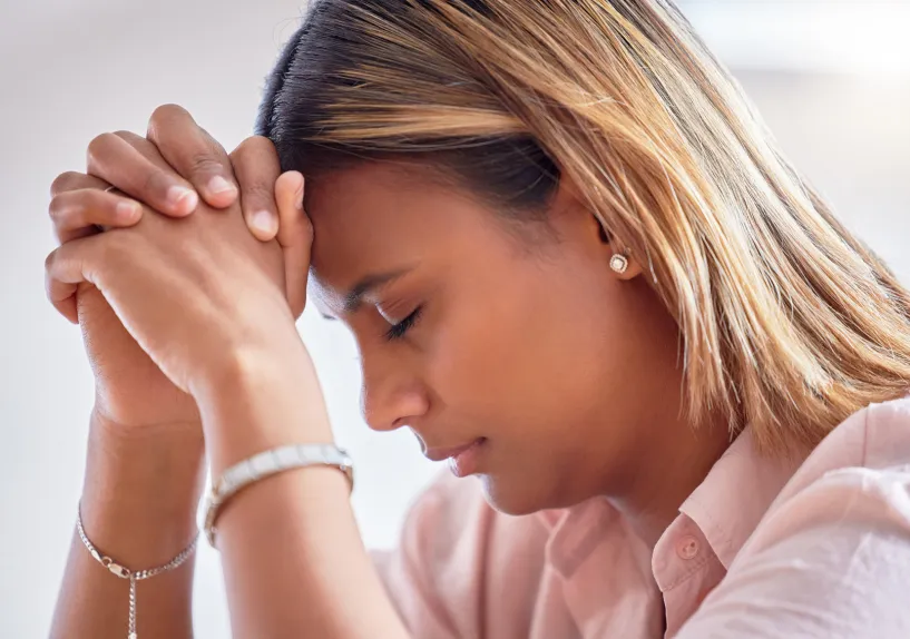 Close‑up of a person with hands clasped together near their face and head lowered.