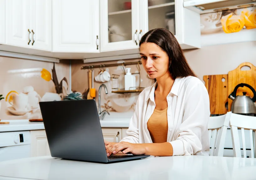 A person sitting at a table in a kitchen using a laptop.