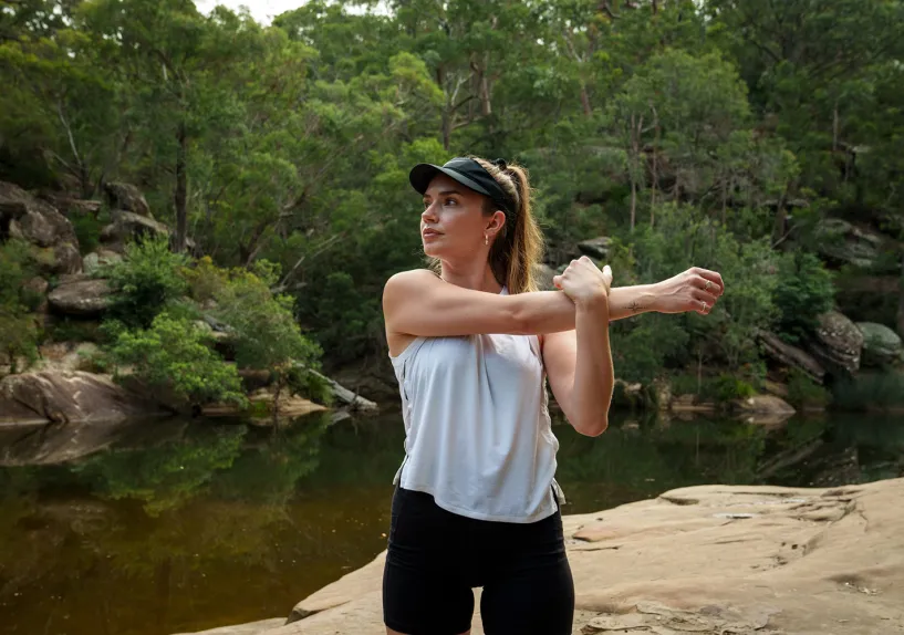 A woman stretching her arm by a creek. 