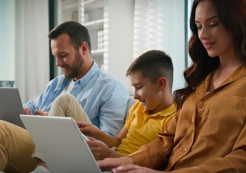A photo of a family sitting on a couch looking at their laptops.