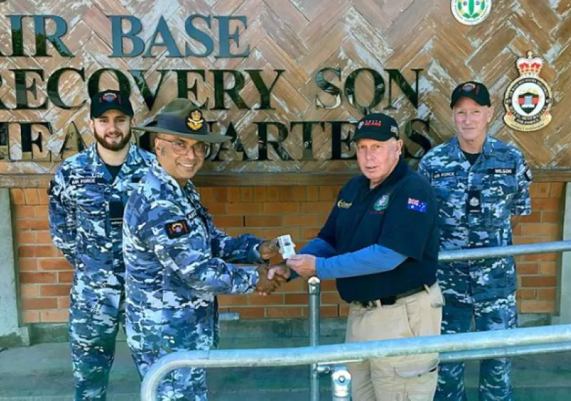 A man shaking hands with an Australian Defence Force member in front of a sign that says 'Air Base Recovery Squadron.'
