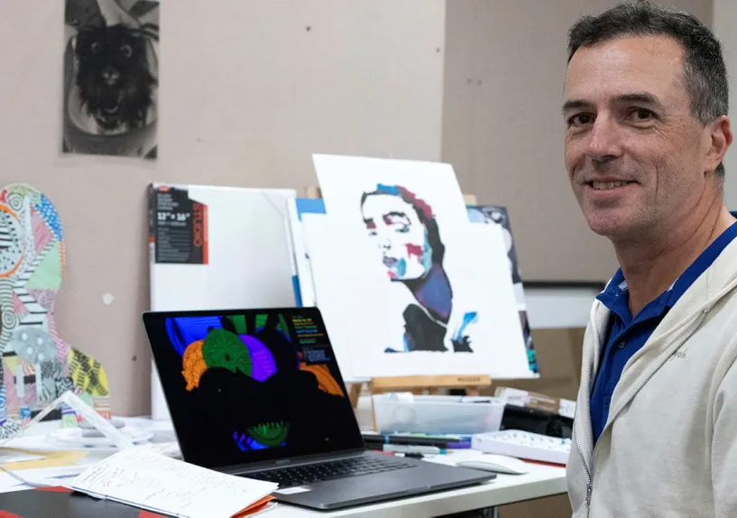 A man smiling sitting in front of artwork.